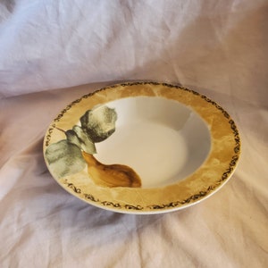 May include: A white ceramic bowl with a brown and green pear design. The bowl has a decorative gold rim with a black floral pattern.
