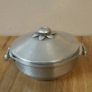 May include: A silver aluminum casserole dish with a lid. The lid has a decorative flower-shaped knob.