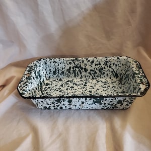 Puede incluir: Un molde para hornear de esmalte blanco y verde moteado con un borde negro. El molde tiene dos pequeñas asas a los lados.