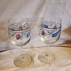 May include: Two clear glass wine glasses with blue, green, and red floral designs. The glasses have a delicate stem and a round base.