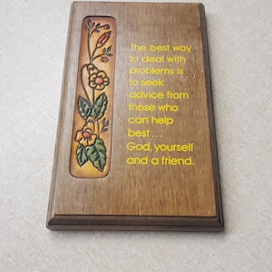 May include: A wooden plaque with a leather inlay featuring a floral design. The plaque has a yellow inscription that reads: "The best way to deal with problems is to seek advice from those who can help best... God, yourself and a friend."