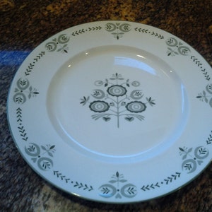 May include: A white ceramic dinner plate with a green floral design. The plate has a scalloped edge and a raised rim.