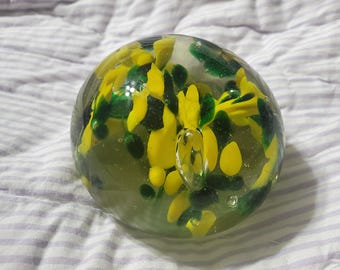 Puede incluir: Un pisapapeles de vidrio transparente con diseños florales amarillos y verdes en su interior.