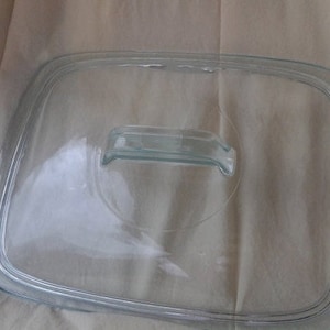 Puede incluir: Una tapa de vidrio transparente con un asa para una fuente para hornear. La tapa es ligeramente curva y tiene una superficie lisa.