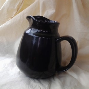 May include: A black ceramic jug with a rounded body and a handle. The jug has a glossy finish.