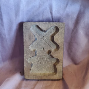 May include: A wooden cookie cutter in the shape of a person with a windmill on their head. The cutter is worn and has a rustic look.
