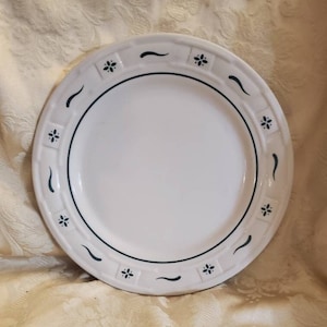 May include: White ceramic dinner plate with a dark blue border and decorative floral and curved line accents. The plate has a slightly raised rim with a repeating pattern of small flowers and curved lines. A simple and elegant design.