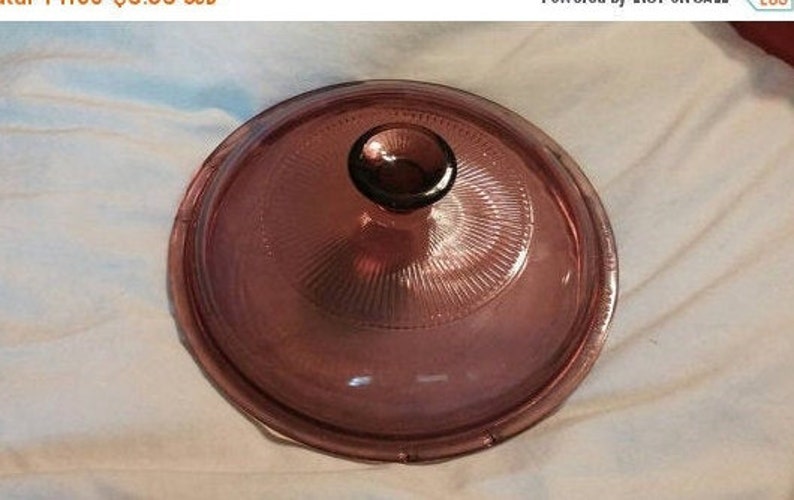 May include: A clear glass lid with a purple hue and a knob on top. The lid has a textured, ribbed pattern.