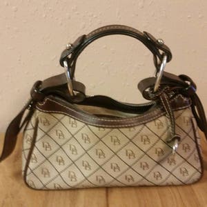 May include: A brown and beige handbag with a brown leather handle and a brown leather strap. The bag has a pattern of small brown and beige squares with a white letter 'B' in each square.
