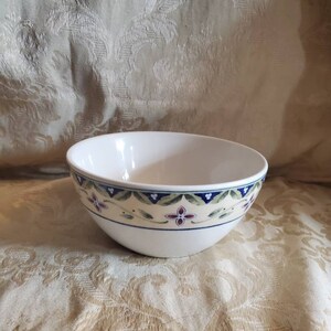 May include: White ceramic bowl with a floral design in shades of blue, green, and pink. The bowl has a scalloped rim and a wide base.