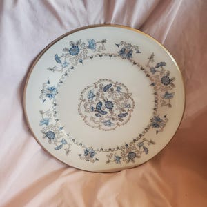 Può includere: Un piatto da portata in ceramica bianca con un bordo dorato e un motivo floreale blu e oro.