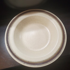 Può includere: Una ciotola in ceramica bianca con un bordo marrone. La ciotola ha una glassa macchiata e un design semplice.