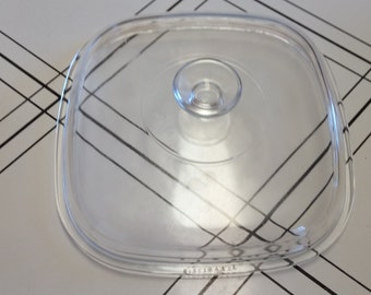 May include: Clear glass lid for a square baking dish with a knob in the center. The lid has the word "Pyrex" printed on the bottom.