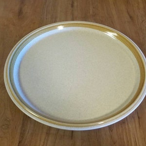May include: A large, round, beige ceramic serving platter with a brown rim.