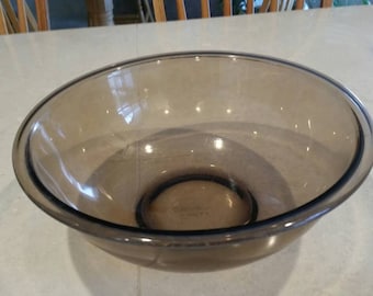 May include: A large, clear glass mixing bowl with a brown tint. The bowl is round and has a wide rim.