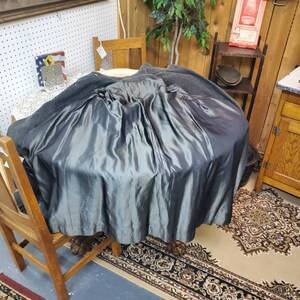 May include: A dark gray wool coat with a satin lining. The coat is turned inside out and draped over a wooden chair. The coat is in a room with a wooden floor and a rug.