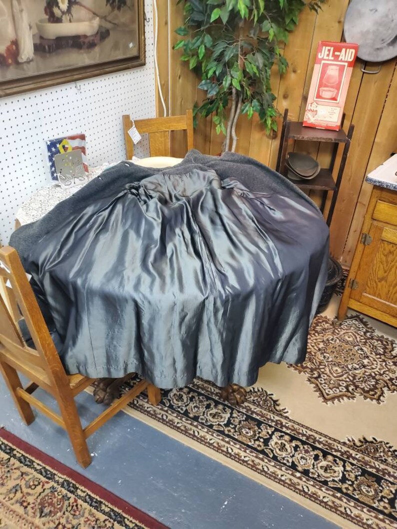May include: A dark gray wool coat with a satin lining. The coat is turned inside out and draped over a wooden chair. The coat is in a room with a wooden floor and a rug.