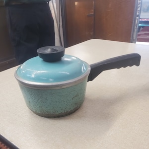 May include: A teal blue vintage saucepan with a black handle and a black lid. The saucepan has a speckled finish.