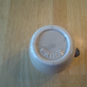 Puede incluir: Taza de cer&aacute;mica blanca con asa marr&oacute;n. En la parte inferior de la taza est&aacute; impresa la palabra "China".