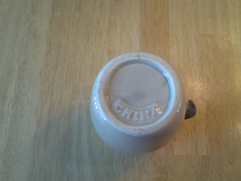 Puede incluir: Taza de cer&aacute;mica blanca con asa marr&oacute;n. En la parte inferior de la taza est&aacute; impresa la palabra "China".