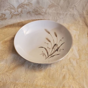 Puede incluir: Un tazón de cerámica blanca con un borde dorado y un diseño de trigo marrón y blanco.