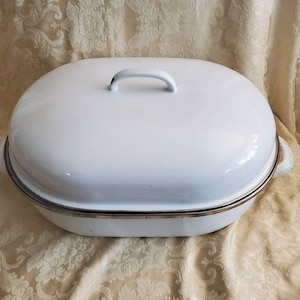 May include: White enamel oval roasting dish with a lid and a handle. The dish has a silver rim around the edge.