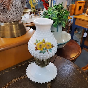 May include: White milk glass lamp with a floral design featuring yellow roses. The lamp has a textured, beaded surface and a metal base.