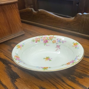 Pode incluir: Uma tigela de cerâmica branca com uma borda dourada e um padrão floral em tons de rosa, laranja e amarelo.