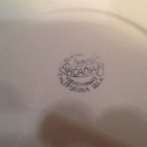 Puede incluir: Primer plano de un plato de cer&aacute;mica blanco con un sello negro que dice "Hand Painted Arcadia Vernonware California USA".