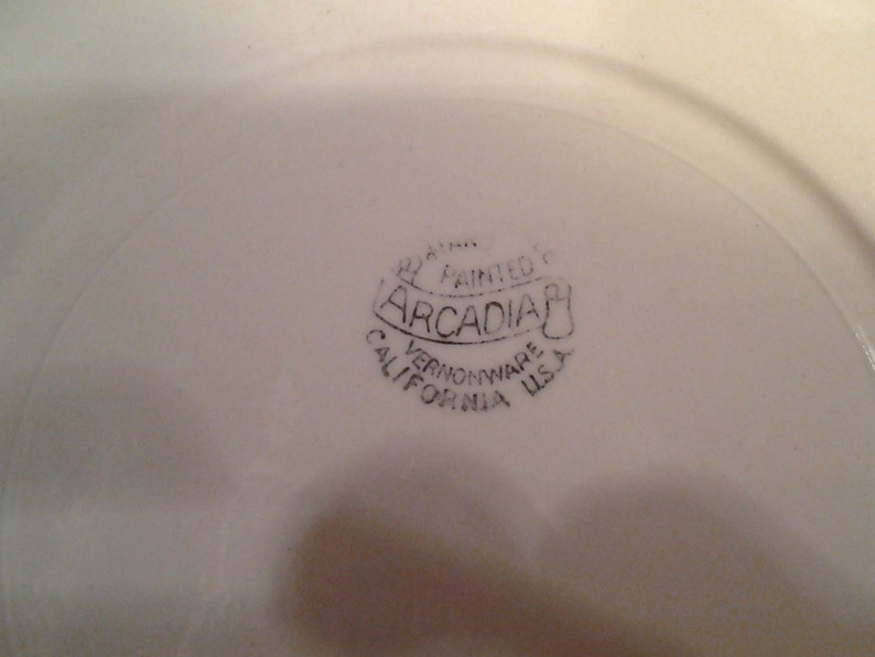 Puede incluir: Primer plano de un plato de cer&aacute;mica blanco con un sello negro que dice "Hand Painted Arcadia Vernonware California USA".