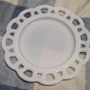 May include: White milk glass plate with a scalloped edge. The plate has a raised design around the edge.