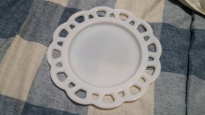 May include: White milk glass plate with a scalloped edge. The plate has a raised design around the edge.