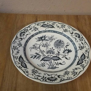 May include: A white ceramic dinner plate with a black floral design. The plate has a scalloped edge and a raised rim.