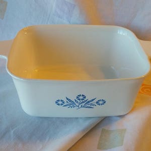 Puede incluir: Plato para hornear de cerámica blanca con diseño floral azul. El plato tiene forma cuadrada y está vacío.