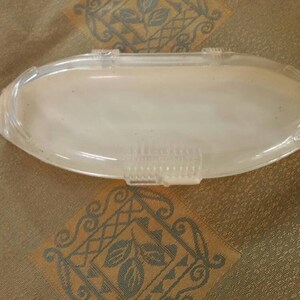 May include: A clear plastic oval-shaped container with a textured surface.