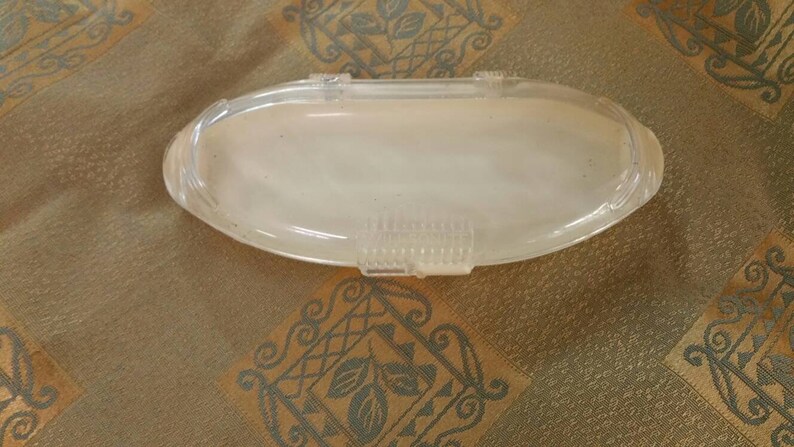 May include: A clear plastic oval-shaped container with a textured surface.