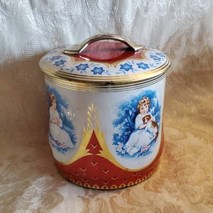 May include: A vintage red, white, and blue tin cookie jar with a gold handle and a floral design. The jar features two images of girls with dogs in a woodland setting.