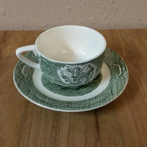 Puede incluir: Un juego de taza y platillo de té verde y blanco con un diseño decorativo. El platillo tiene un borde verde con un centro blanco y un diseño verde en el centro. La taza de té tiene un interior blanco y un exterior verde con un diseño blanco en el centro.