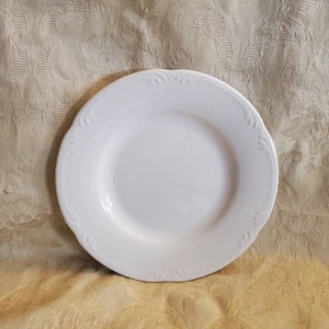 May include: A white ceramic plate with a scalloped edge and a simple design. The plate is perfect for serving a small meal or snack.