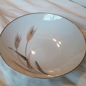 May include: A white ceramic bowl with a gold rim and a design of wheat stalks in brown and gold.