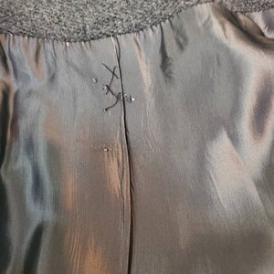 May include: Close-up of the inside seam of a black coat. The seam is sewn with black thread and is visible through the lining.