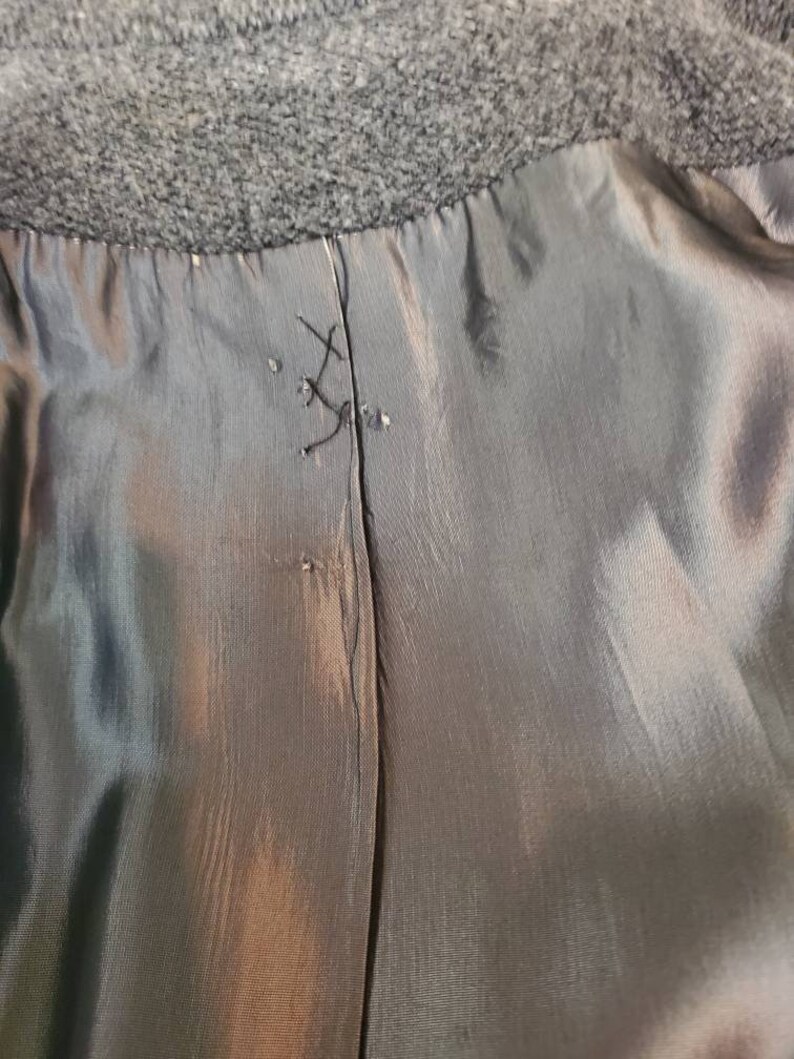 May include: Close-up of the inside seam of a black coat. The seam is sewn with black thread and is visible through the lining.