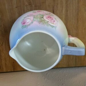 May include: A blue and white ceramic jug with a floral design featuring pink roses. The jug has a handle and a spout.