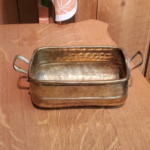 May include: A hammered brass planter with two handles. The planter is rectangular and has a slightly rounded bottom.