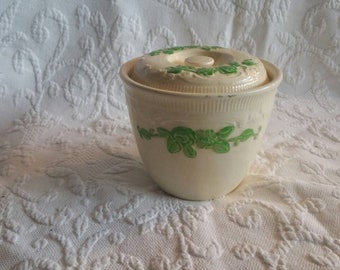 May include: A white ceramic jar with a lid, decorated with green floral designs. The jar has a smooth, rounded shape and a slightly flared rim.