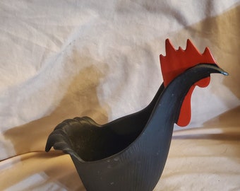 Peut inclure: Un pot en forme de coq noir avec une crête rouge. Le pot a une surface texturée et un design incurvé, ressemblant au corps d'un oiseau. Le pot est probablement en céramique ou dans un matériau similaire.