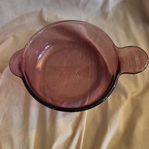 Può includere: Una pirofila di vetro viola con due manici. La pirofila è realizzata da CorningWare.