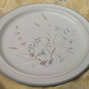 May include: A white ceramic dinner plate with a light blue rim. The plate features a delicate floral design with a light brown and gray color scheme.
