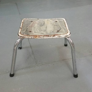 May include: A white metal step stool with chrome legs. The stool has a slightly curved top and a textured surface.