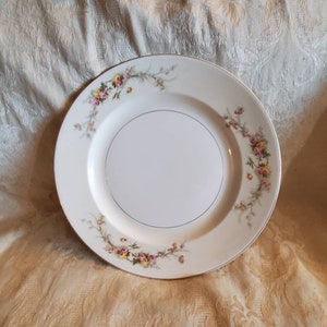 Può includere: Un piatto da portata in ceramica bianca con un bordo dorato e un motivo floreale con fiori rosa, gialli e verdi.